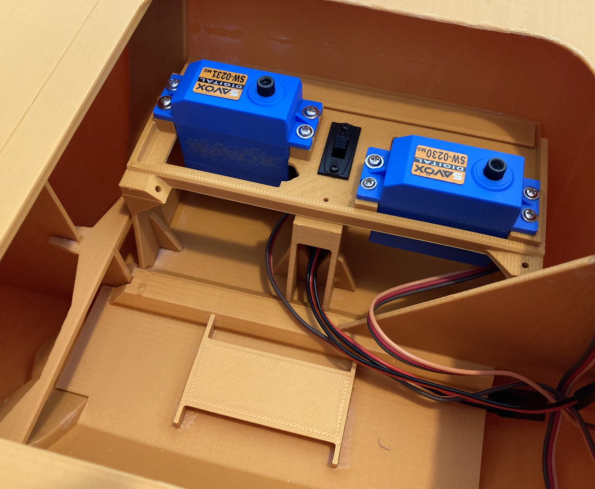Nahaufnahme eines 3D-gedruckten Modellboot-Innenraums, der zwei montierte Savox-Digitalservos (SW-0231MG und SW-0230MG) zeigt, die auf einem gedruckten Servo-Tray gesichert sind. Ein kleiner schwarzer Schalter befindet sich zwischen den Servos, und die Se