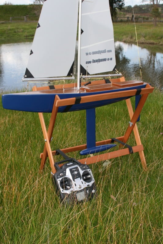 A racing sparrow model yacht sitting a cradle next to the lake
