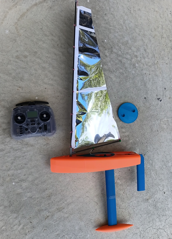 Racing Sparrow Footy V1 3D printed RC sailboat side view with reflective sail and radio controller beside it