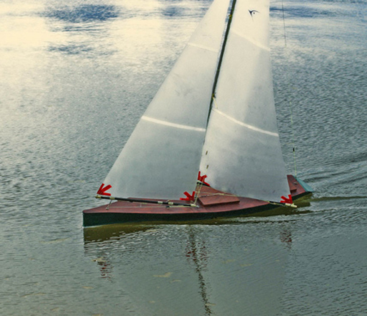 RS1000 model yacht, dark green hull with white translucent sails, smoothly sailing fast through the calm green water. Looks almost like a vintage photograph from times gone by, Location: Sydney, Australia