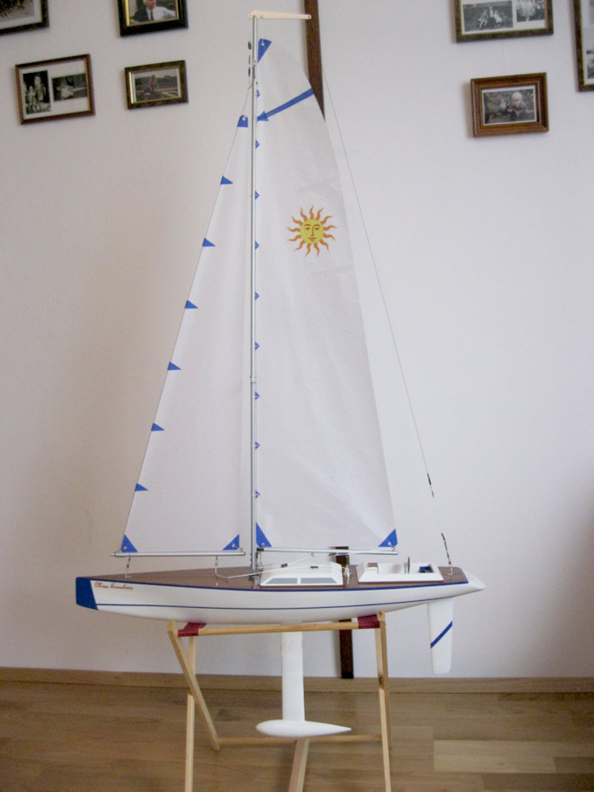 A white model racing sparrow yacht, sitting on a cradle inside against a white wall and wooden floor, Location: Vienna, Austria