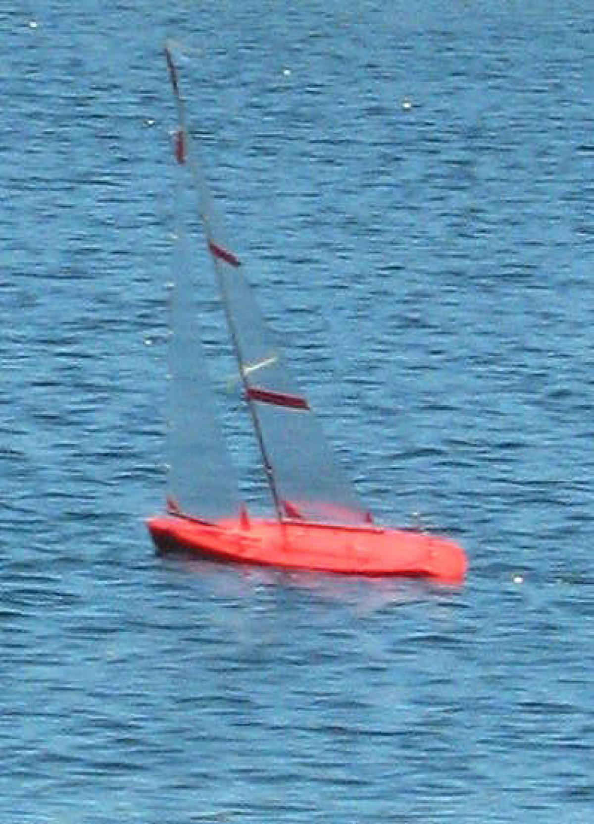 a red model yacht sailing upwind on flat waters, Location: Perth, Western Australia