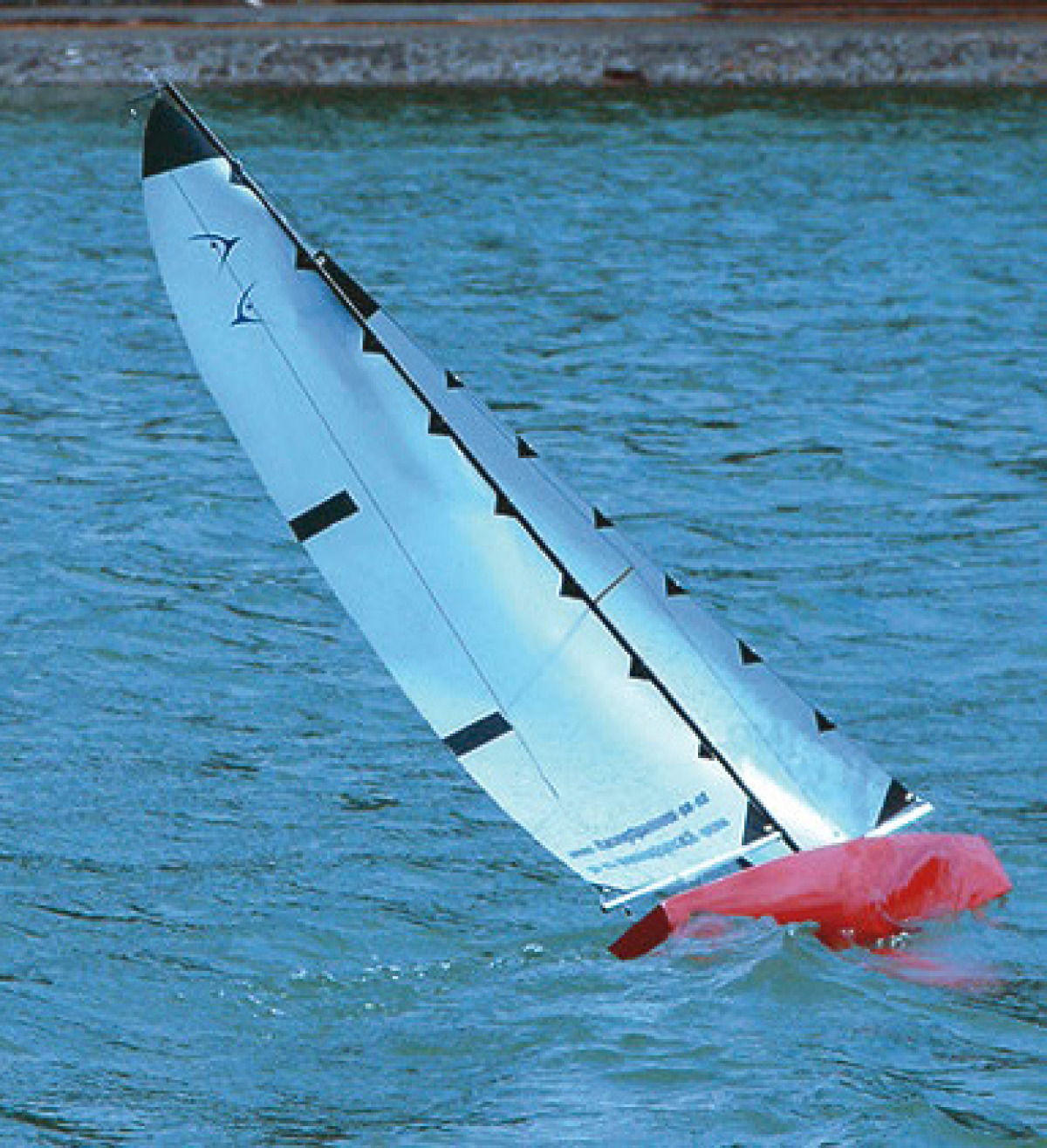 a shiney red radio controlled yacht called a Racing Sparrow sailing upwind and leaning over 45 degrees