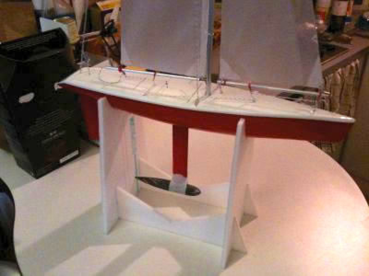 A small rc yacht red in colour sitting in a small styrene cradle on a table