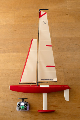 A red 3D printed model yacht from Racing Sparrow in New Zealand. An ideal project for the 3D printing enthusiast. The image shows a rc controller and a two sailed model sailboat.
